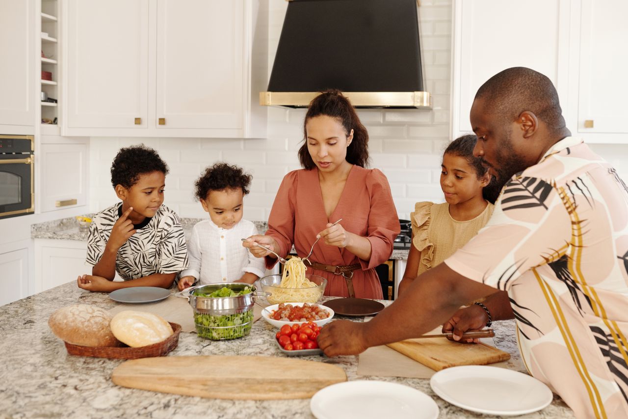 A diverse family prepares pasta in a modern white kitchen, conveying unity and culinary art.